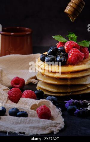 Pfannkuchen mit Beeren und Honig auf dunklem Hintergrund Stockfoto