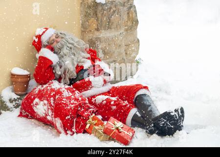 Der Weihnachtsmann schläft im Schnee und lehnt sich an das Haus Stockfoto