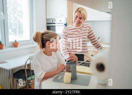 Mutter und Tochter genießen die warme Zeit zusammen in der modernen Küche, die Mahlzeiten zubereiten. Die Tochter lächelt herzlich, wenn sie dieses Kocherlebnis teilen. Perfekt für Stockfoto