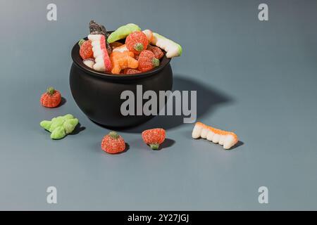 Bunte Auswahl an gummiartigen Halloween-Bonbons in einer schwarzen Kaldron-Schüssel auf blauem Hintergrund Stockfoto