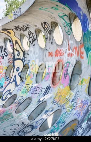 Betonwand mit kreisrunden Löchern und Grafitti im Sonnenschein Stockfoto