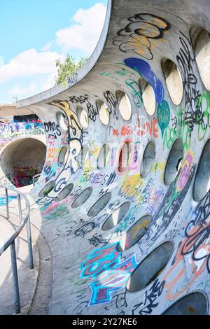 Betonwand mit kreisrunden Löchern und Grafitti im Sonnenschein Stockfoto