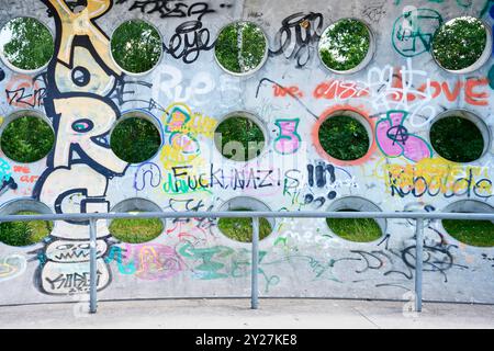 Betonwand mit kreisrunden Löchern und Grafitti im Sonnenschein Stockfoto