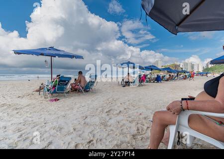 Guaruja, SP, Brasilien - 12. April 2024: Vormittag am Enseada Beach mit ein paar Badenden bereits unter den Sonnenschirmen. Stockfoto