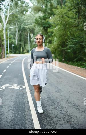 Eine junge Frau trainiert selbstbewusst im Freien, indem sie ihre Beinprothese benutzt, während sie Musik hört. Stockfoto