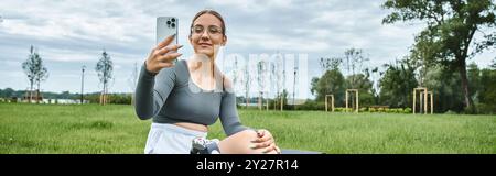 Eine junge Frau mit einer Beinprothese lächelt, während sie ein Selfie während ihres Outdoor-Workouts macht. Stockfoto