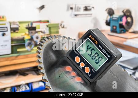 Nahaufnahme des digitalen Neigungsmessers des Messwerkzeugs an der Metallscheibe der Kreissäge. Messung des Neigungswinkels mit elektronischem Instrument im Hintergrund des Arbeitsraums. Stockfoto