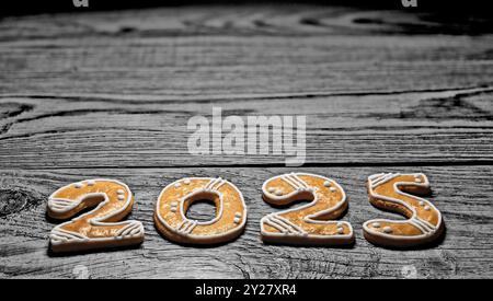 Großaufnahme von goldenen Lebkuchen für 2025 frohe Neujahrsgrüße auf dunklem Holz. Verzierte süße Weihnachtskekse auf schwarzweißem natürlichen Hintergrund. Stockfoto