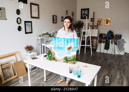 Künstlerin mit Kunstharzkunst Küstenlandschaft, kreatives Heimstudio, handgemachte Strandszene, künstlerischer Arbeitsbereich, DIY Epoxidkunst, von der Natur inspiriert Stockfoto