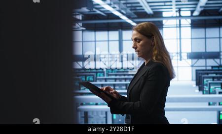 Computerwissenschaftler, der die Überprüfung durchführt und Daten auf Tablets mit den erforderlichen Fehlerbehebungen im Server-Hub eingibt. Frau, die im Rechenzentrum arbeitet und eine fortschrittliche Datenspeicherinfrastruktur zur Unterstützung von IT-Workloads bietet, Kamera A Stockfoto