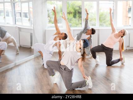 Mädchen und ihre Schüler führen Hip-Hop-Tanz auf einem gebogenen Bein auf, Bewegung in horizontaler Ebene in Bodennähe Stockfoto