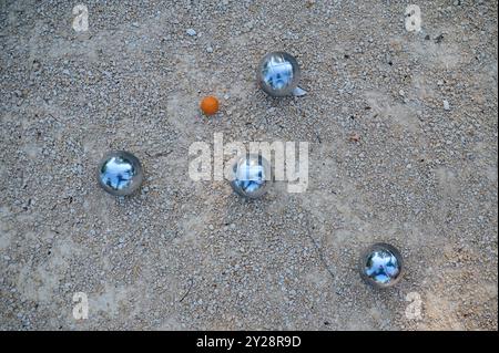 Nahaufnahme von Petanque-Kugeln, die auf Kies verstreut sind, mit dem Zielball im Fokus. Die glänzenden Metallkugeln reflektieren das Sonnenlicht und halten eine verspielte Outdoor-Atmosphäre fest Stockfoto