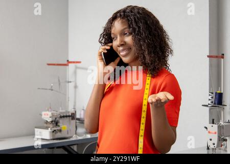 Schneiderin spricht über Smartphone mit Kunden, die Arbeiten und Kundenbestellungen verwalten Stockfoto