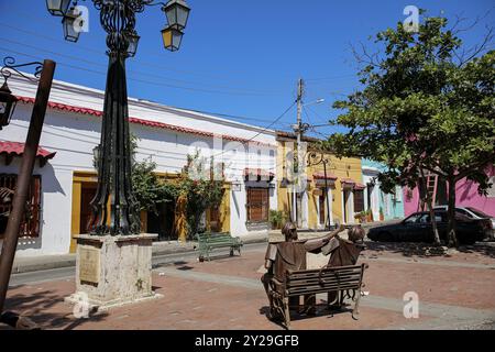 Kleiner Platz mit grünen Bäumen und Laternenmast im Gethsemane-Viertel von Cartagena, eingerahmt von bunten einstöckigen Häusern an einem sonnigen Tag, Colombi Stockfoto