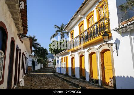 Enge Straße mit einem wunderbaren Kolonialgebäude mit gelben Holztüren, Fenstern und Balustrade in der späten Nachmittagssonne, historische Stadt Paraty, Brasilien, Stockfoto