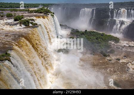 Blick auf die mächtigen Iguazu-Fälle in der Nähe von Devil's Throat mit braunem und weißem Wasser in üppiger grüner Vegetation Stockfoto