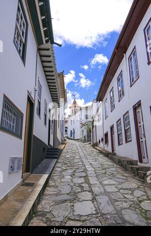 Enge Kopfsteinpflasterstraße mit traditionellen Häusern, blauem Himmel und weißen Wolken in Diamantina, Minas Gerais, Brasilien, Südamerika Stockfoto