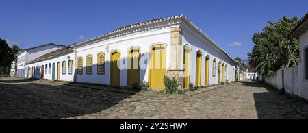 Eckblick auf ein weiß-gelbes Kolonialhaus mit Schatten auf einer Kopfsteinpflasterstraße an einem sonnigen Tag in der historischen Stadt Paraty, Brasilien, UNESCO World Heri Stockfoto