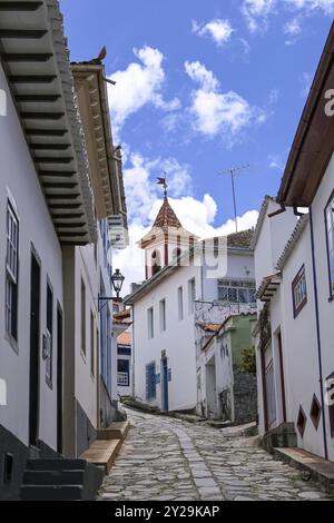 Enge Kopfsteinpflasterstraße mit traditionellen Häusern, blauem Himmel und weißen Wolken in Diamantina, Minas Gerais, Brasilien, Südamerika Stockfoto