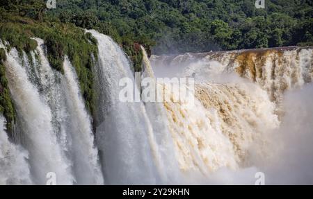 Nahaufnahme der mächtigen Iguazu-Fälle mit weißem, grauem und braunem Wasser und grüner Vegetation im Sonnenlicht Stockfoto