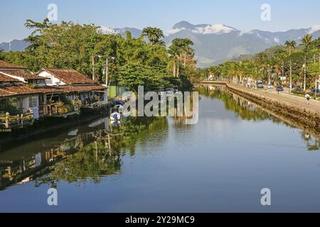 Blick auf den Fluss Pereque-ACU mit Häusern, Vegetation und Regenwaldbergen im Hintergrund an einem sonnigen Tag, Reflexionen auf dem Wasser in UNESCO World Heri Stockfoto