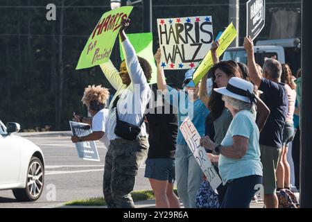 Suwanee, GA / USA - 7. September 2024: Demokratische Aktivisten ermutigen Fahrzeuge, sich die Hörner zu blasen, während sie bei einer Veranstaltung von Honk for Harris Schilder hochhalten. Stockfoto