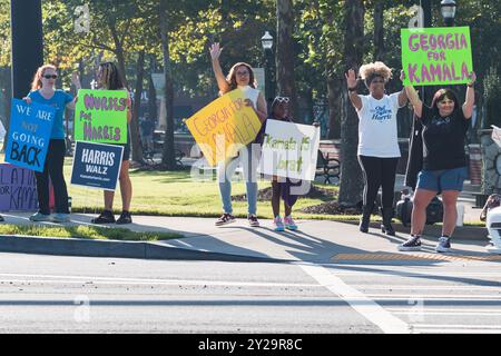 Suwanee, GA / USA - 7. September 2024: Demokratische Aktivisten ermutigen Fahrzeuge, sich die Hörner zu blasen, während sie bei einer Veranstaltung von Honk for Harris Schilder hochhalten. Stockfoto