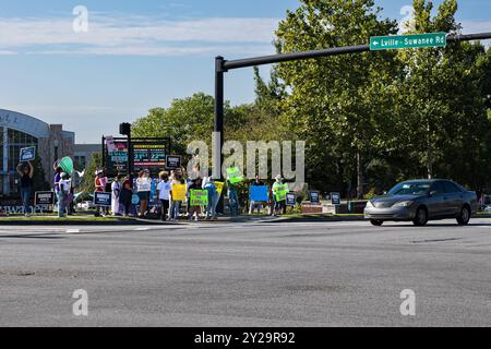 Suwanee, GA / USA - 7. September 2024: Demokratische Parteiaktivisten ermutigen vorbeifahrende Fahrzeuge, sich bei einer Veranstaltung „Honk for Kamala Harris“ die Hörner zu blasen. Stockfoto