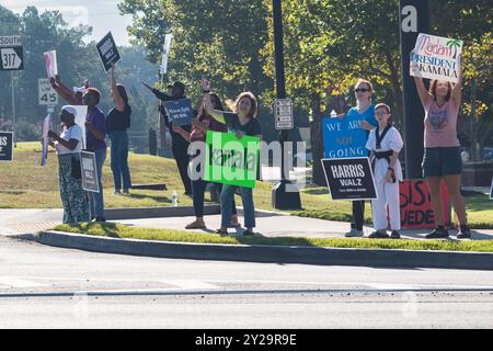 Suwanee, GA / USA - 7. September 2024: Freiwillige demokratischer Parteien ermutigen vorbeifahrende Fahrzeuge, sich bei einer lokalen Veranstaltung von Honk for Harris die Hörner zu blasen. Stockfoto