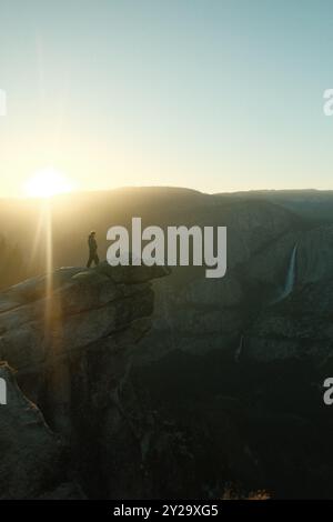 Person, die auf einem Felsvorsprung mit Wasserfall und Sonnenuntergang im Yosemite National Park, Kalifornien, steht Stockfoto