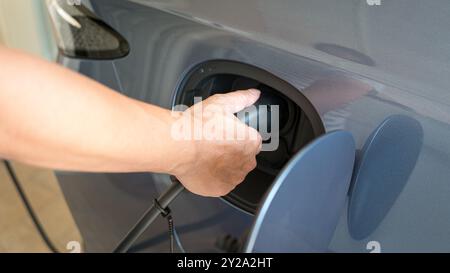 Mann, der sein Elektroauto auflädt. Nahaufnahme des Einsteckens des elektrischen Steckverbinders am Fahrzeug. Stockfoto