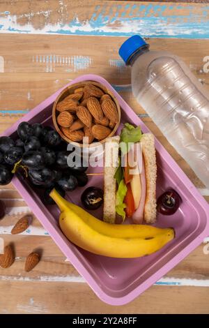 Präsentation des Mittagessens in der Schule. Draufsicht mit einer umweltfreundlichen Lunchbox gefüllt mit nahrhaften Lebensmitteln, Proteinen, Früchten und Körnern Stockfoto