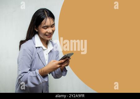 Porträt einer Büroangestellten, die Nachrichten auf ihrem Mobiltelefon beantwortet. Sie ist eine Frau, die ein langes, glattes blaues Hemd trägt, isoliertes leeres c Stockfoto