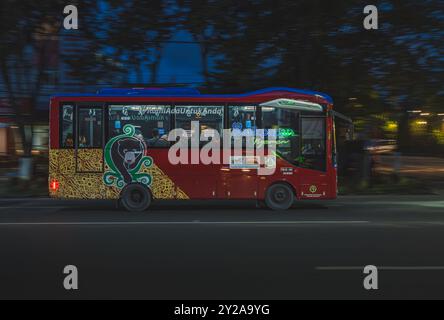 Balikpapan, Indonesien - 9. August 2024. Ein Balikpapan City Trans Bus in Rot fährt nachts durch eine geschäftige Stadtstraße, beleuchtet von City Long Stockfoto
