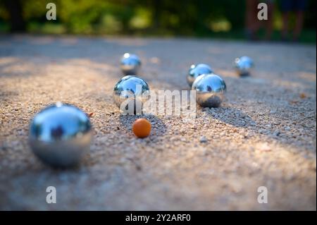 Nahaufnahme von Petanque-Kugeln, die auf Kies verstreut sind, mit dem Zielball im Fokus. Die glänzenden Metallkugeln reflektieren das Sonnenlicht und halten eine verspielte Outdoor-Atmosphäre fest Stockfoto