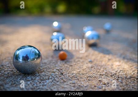 Nahaufnahme von Petanque-Kugeln, die auf Kies verstreut sind, mit dem Zielball im Fokus. Die glänzenden Metallkugeln reflektieren das Sonnenlicht und halten eine verspielte Outdoor-Atmosphäre fest Stockfoto