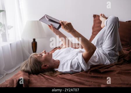 Ältere Frau, die im Bett liegt und während einer friedlichen Morgenroutine ihr Tagebuch liest, über Gedanken nachdenkt, den Tag ruhig beginnt und es genießt Stockfoto