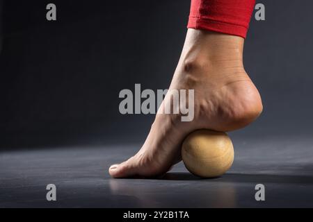 Myofasziale Freisetzung der Fussmuskeln mit Massageball auf dunklem Hintergrund, Nahaufnahme. Konzept zum Thema Fussermüdung nach Tragen h Stockfoto