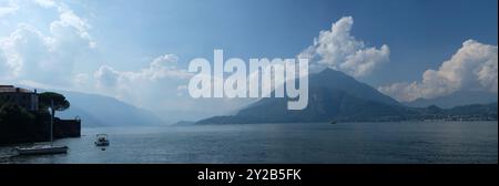 Ein Panoramablick auf den Comer See von den Ufern von Varenna, eine breite Schleife, Wasser und Boote, Berg erhebt sich über Berge, Grate in Nebel und Wolken Stockfoto