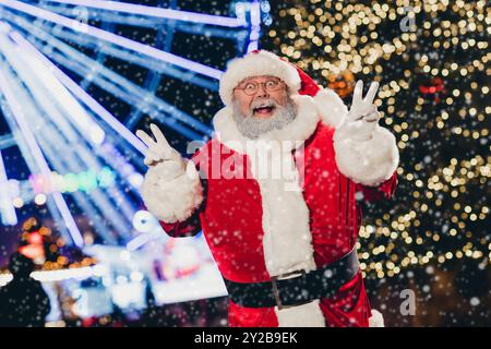 Portrait des aufregenden, flippigen weihnachtsmanns Großvater zwei Hände zeigen V-Schild Genießen Sie die Lichter des Neujahrs draußen Stockfoto