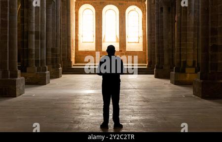 Ein Mann steht in einer großen, leeren Kammer mit einem Fenster im Hintergrund in einem Kloster oder einer Kirche. Das Zimmer ist schwach beleuchtet und der Mann sieht mit Admi Stockfoto