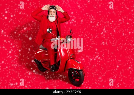 Foto von ziemlich gut aussehend reifen Motorradfahrer gekleidet weihnachten Kostüm Helm Arme Brille isoliert rote Farbe Hintergrund Stockfoto
