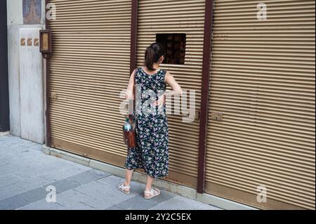 14.06.2019, Wien, Österreich, Europa - Eine Frau steht vor einem geschlossenen Geschäft mit abgesenkten Rollläden in einer Fußgängerzone im Stadtzentrum. Stockfoto