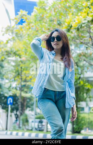 Elegante asiatische Frau in Sonnenbrille kämmt ihr Haar auf einem Outdoor Park Pfad. Studentinnen für die Themen Bildung, Mode und Lifestyle Stockfoto