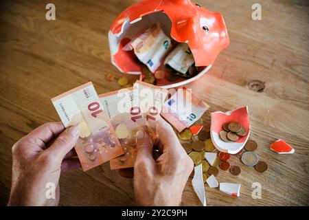 Berlin, Deutschland. September 2024. Symbolfoto zum Thema Finanzen im Alter - Altersarmut. Ein alter Mann sitzt zu Hause am Tisch vor einer kaputten Schweinebank und zählt Geld. Berlin, 5. September 2024. Quelle: dpa/Alamy Live News Stockfoto