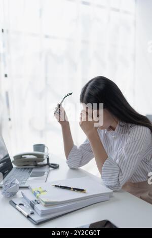 Geschäftsfrau plant eine Finanzprüfung, prüft Dokumente, während sie gegen das Burnout-Syndrom kämpft Stockfoto