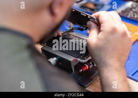 Ein erfahrener Techniker ersetzt in einer Reparaturwerkstatt sorgfältig die Batterie des Telefons, wobei er sich auf Präzision und Detailgenauigkeit konzentriert Stockfoto