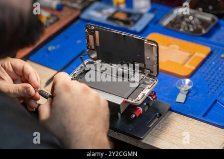 Ein Techniker zerlegt ein Smartphone geschickt, um seinen Akku in einer gut ausgestatteten Reparaturwerkstatt auszutauschen Stockfoto