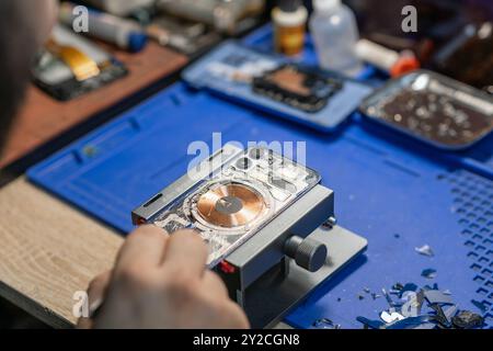 Ein Techniker repariert ein Smartphone sorgfältig und konzentriert sich dabei auf den Batteriewechsel zwischen verschiedenen Werkzeugen und Teilen in der Werkstatt Stockfoto