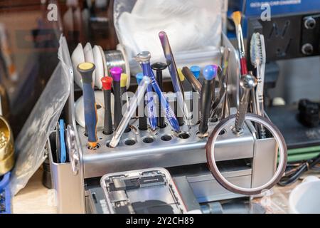 Die Werkzeuge sind ordentlich in einer Reparaturstation organisiert, bereit für Telefonreparaturen und Batteriewechsel in einer belebten Werkstatt Stockfoto